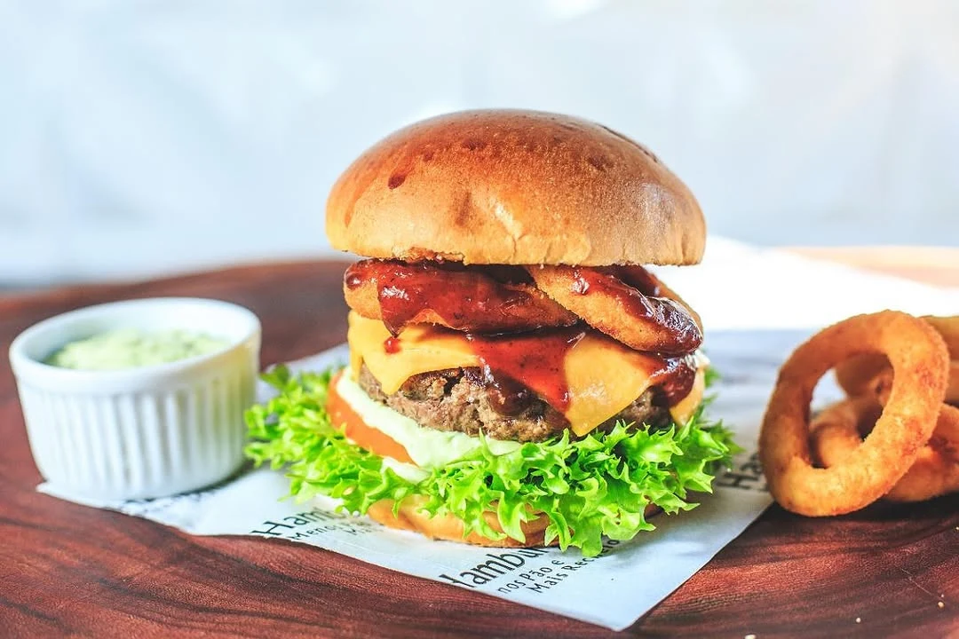 Hambúrguer com bacon e queijo, acompanhado de molho e anéis de cebola